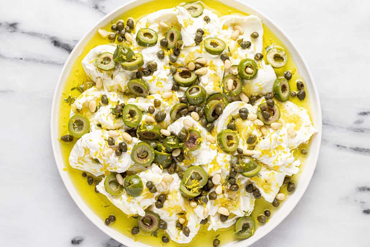 Large serving plate with burrata cheese, garlic olive oil, olives, and pine nuts. 