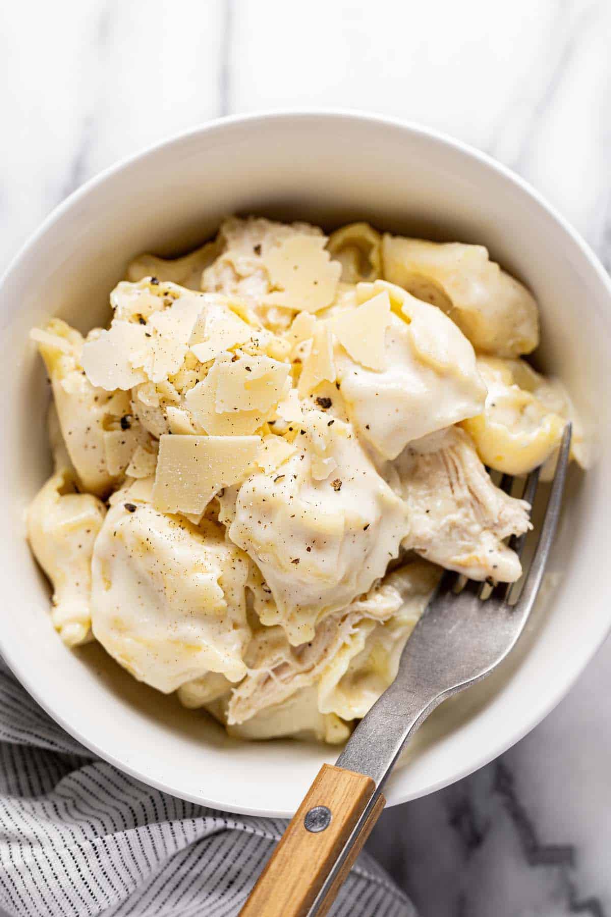 Bowl of chicken alfredo tortellini garnished with Parmesan cheese and black pepper. 