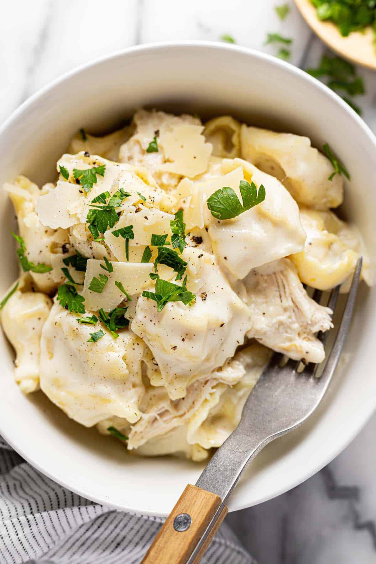 Bowl of chicken tortellini alfredo garnished with Parmesan and parsley. 