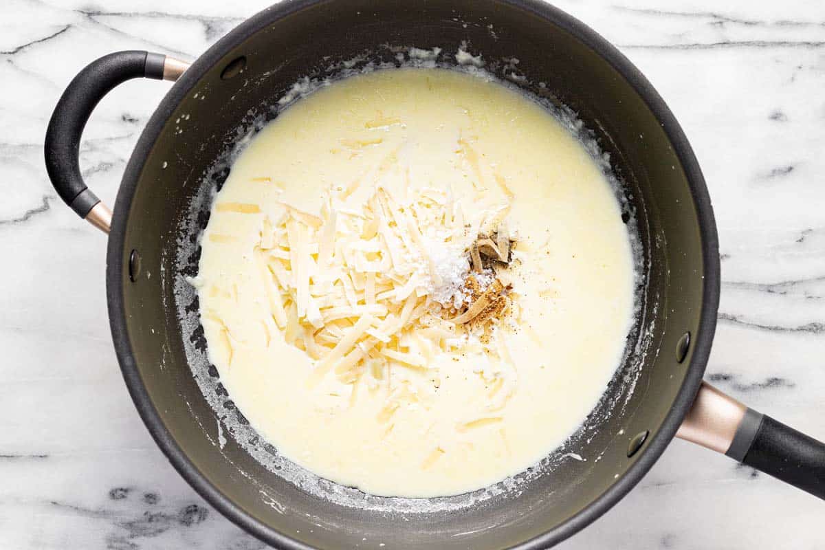 Pan with alfredo sauce in it with Parmesan cheese, salt, pepper, and nutmeg added. 