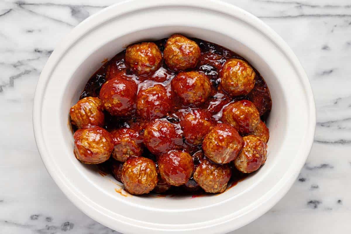 Slow cooker insert with meatballs tossed in cocktail toss. 