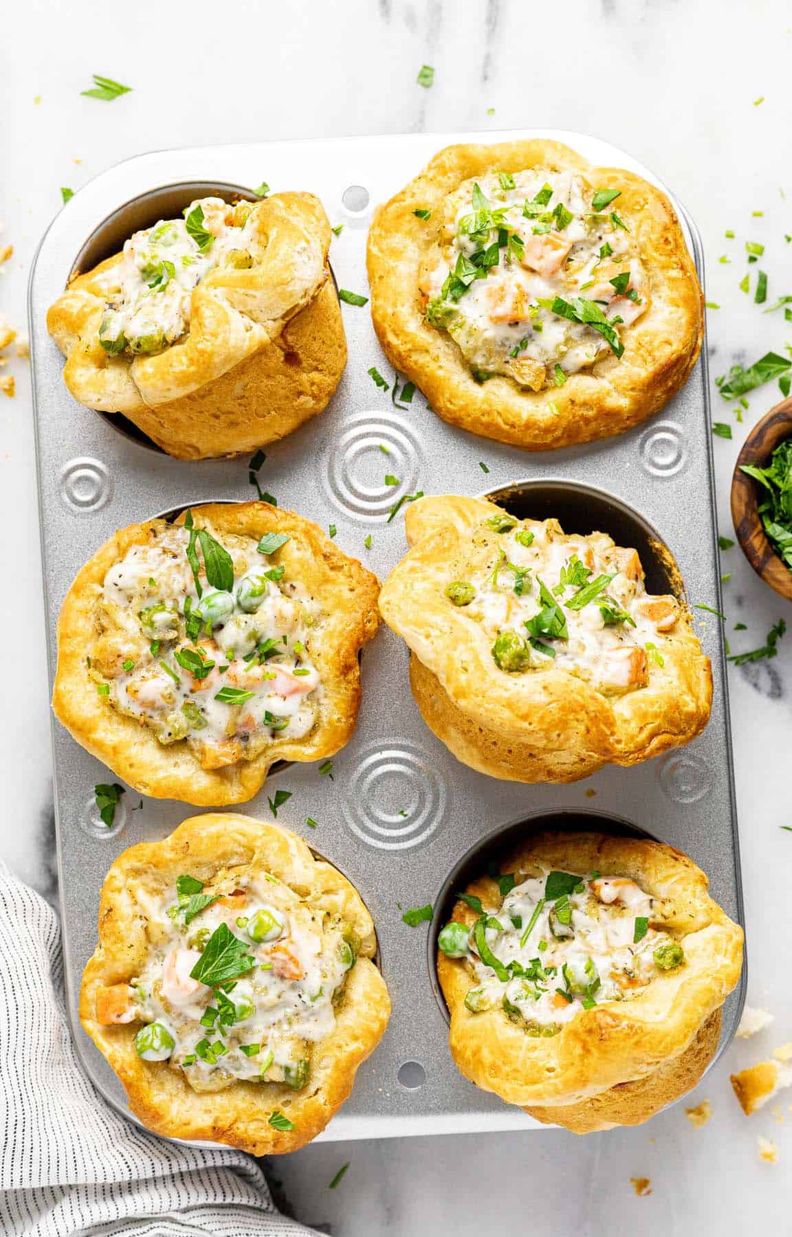 Muffin tin filled with mini chicken pot pies garnished with parsley. 