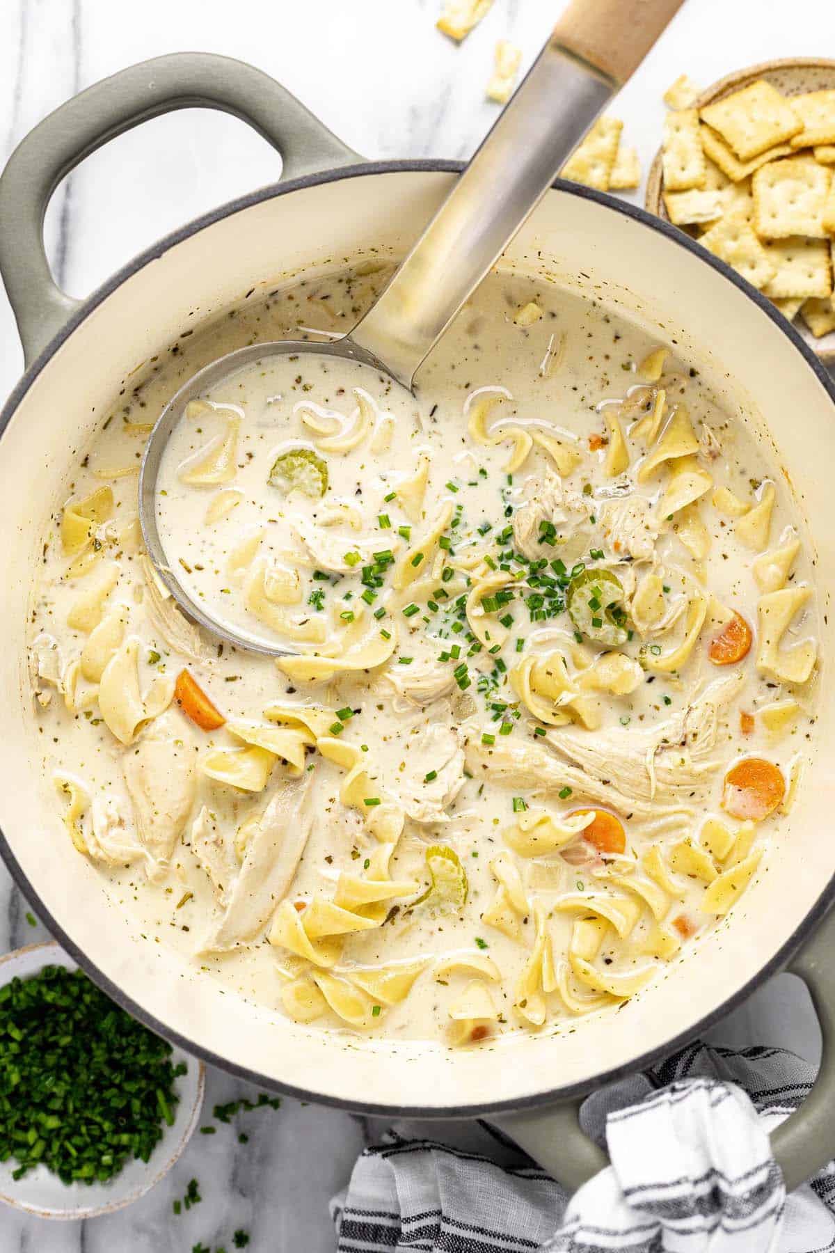 Large pot of rotisserie chicken noodle soup garnished with sliced chives. 