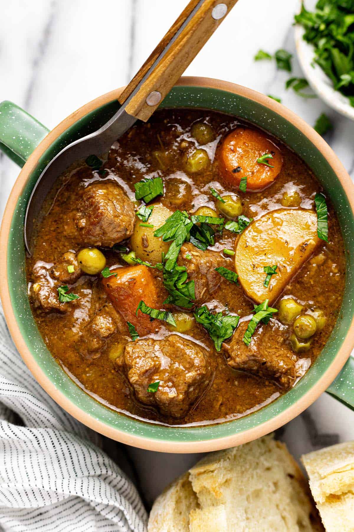 Bowl of homemade beef stew garnished with parsley with a spoon in it. 