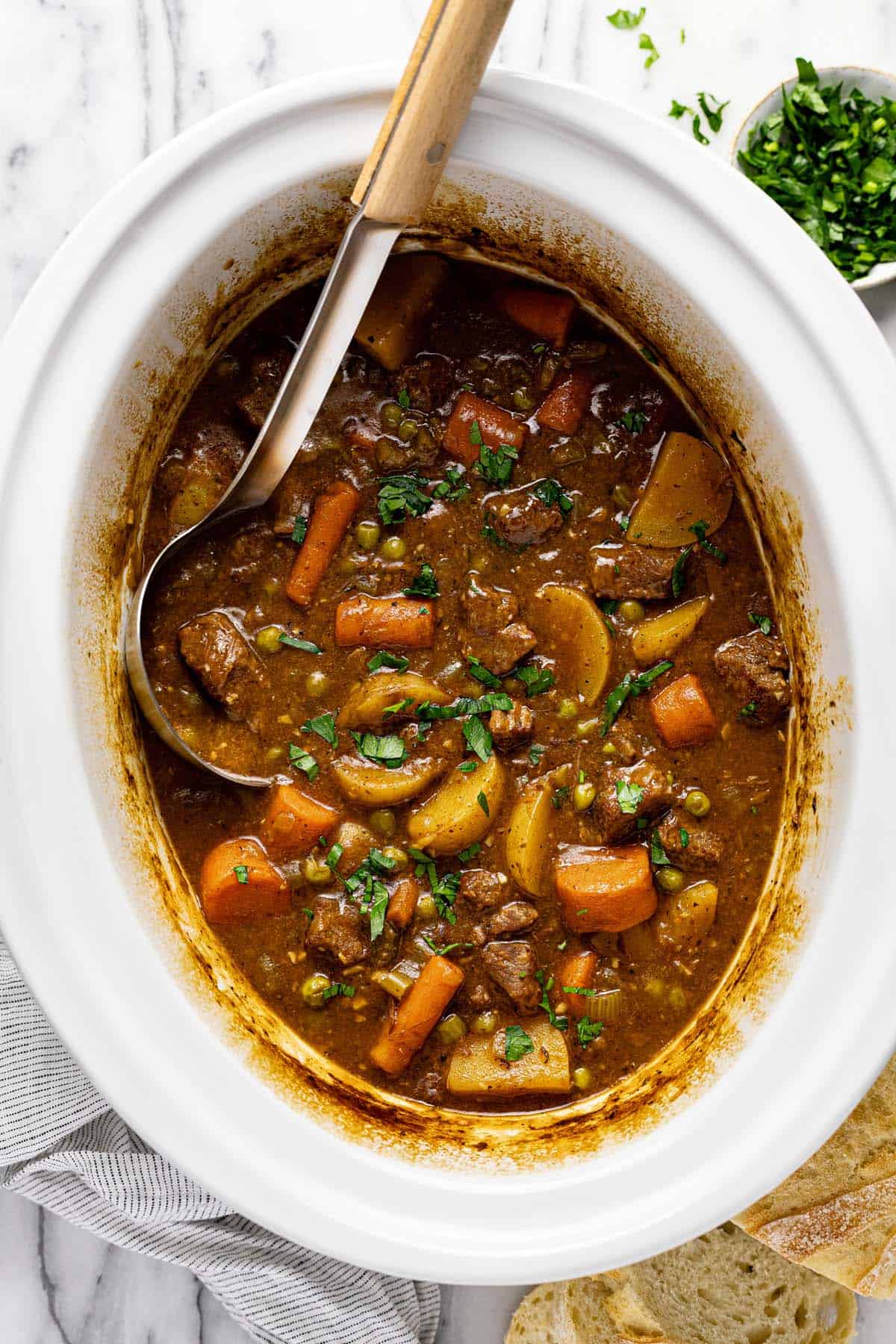 Slow cooker insert filled with beef stew garnished with fresh parsley. 