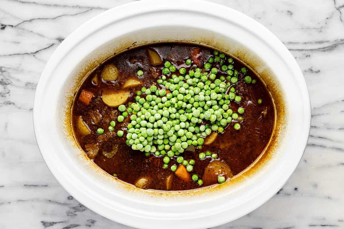 Slow cooker beef stew with frozen peas and a corn starch slurry added on top. 