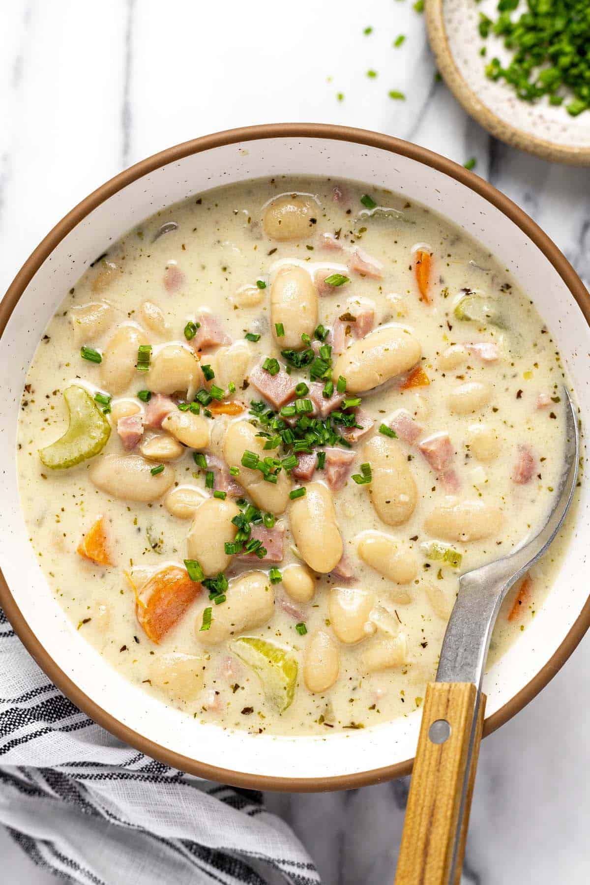 Bowl of white bean and ham soup garnished with sliced chives. 