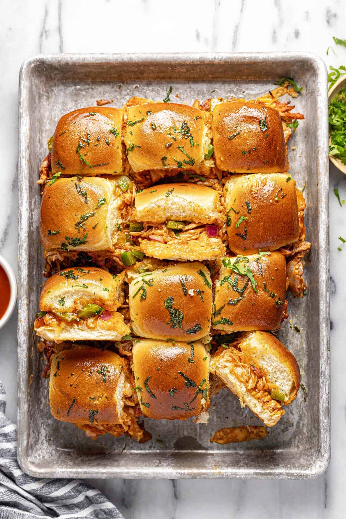 Baking sheet with BBQ chicken sliders topped with cilantro.