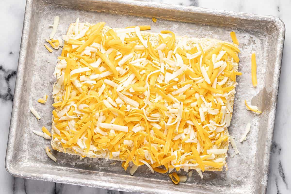 Baking sheet with a slab of rolls topped with shredded cheese. 