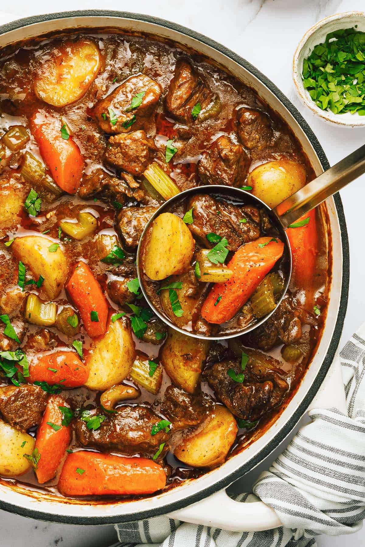 Dutch oven beef stew in a large pot garnished with fresh parsley. 