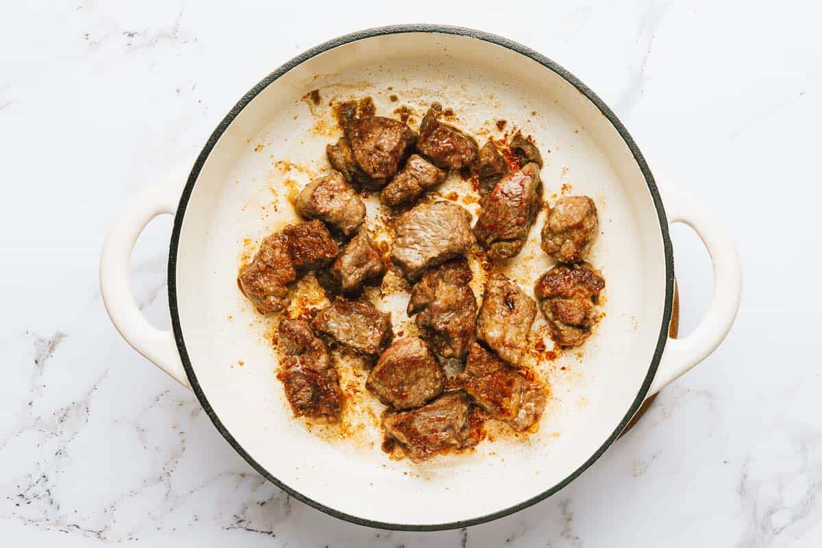 Large pot with seared chunks of beef in it. 