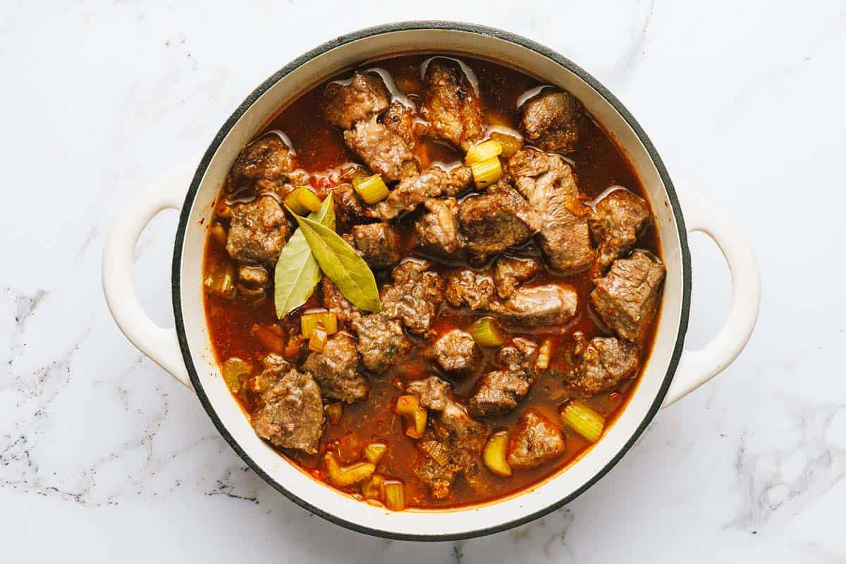 Large pot with stock, seared beef, and veggies. 