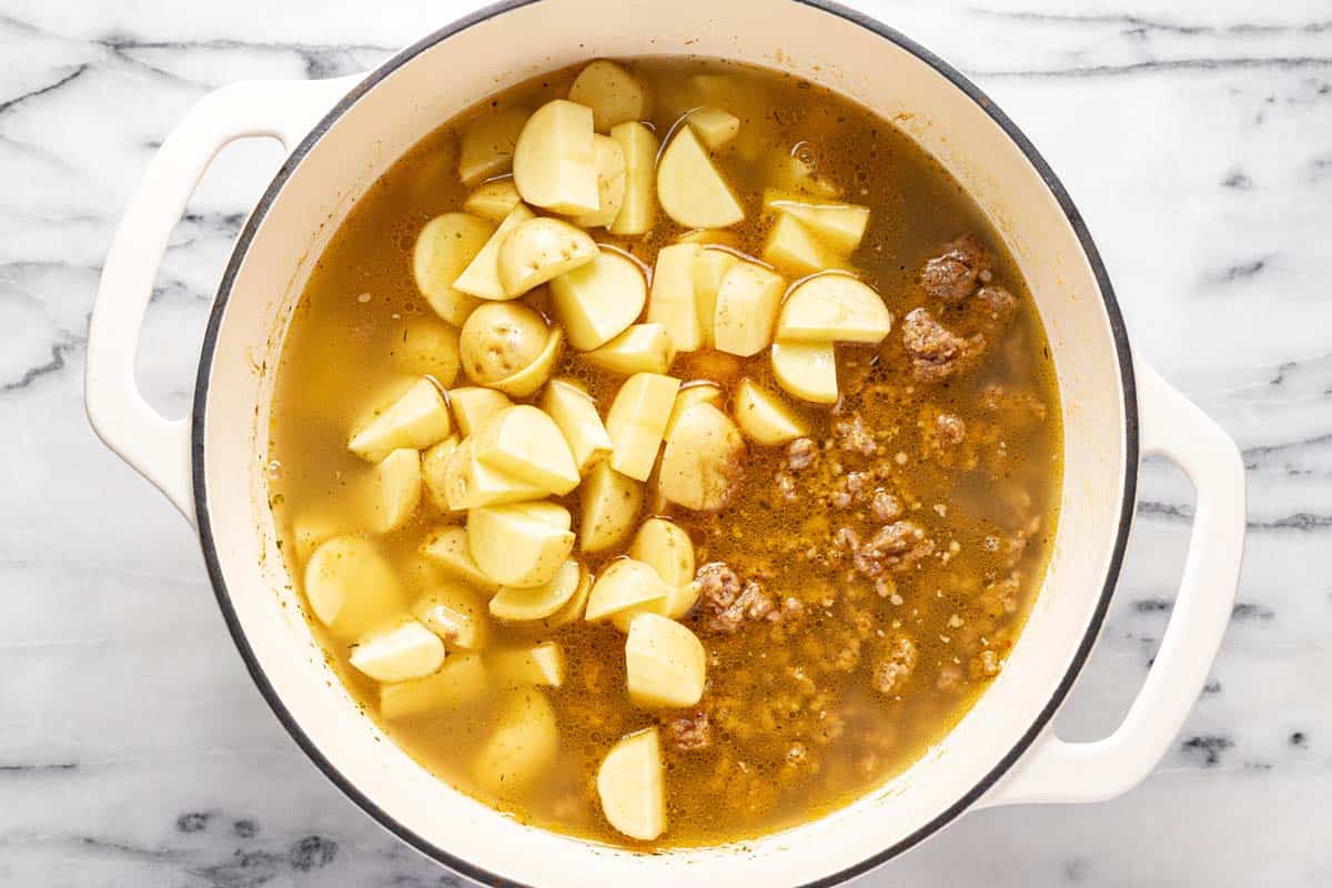 Broth with browned sausage, sauteed veggies, and potatoes in a large pot. 