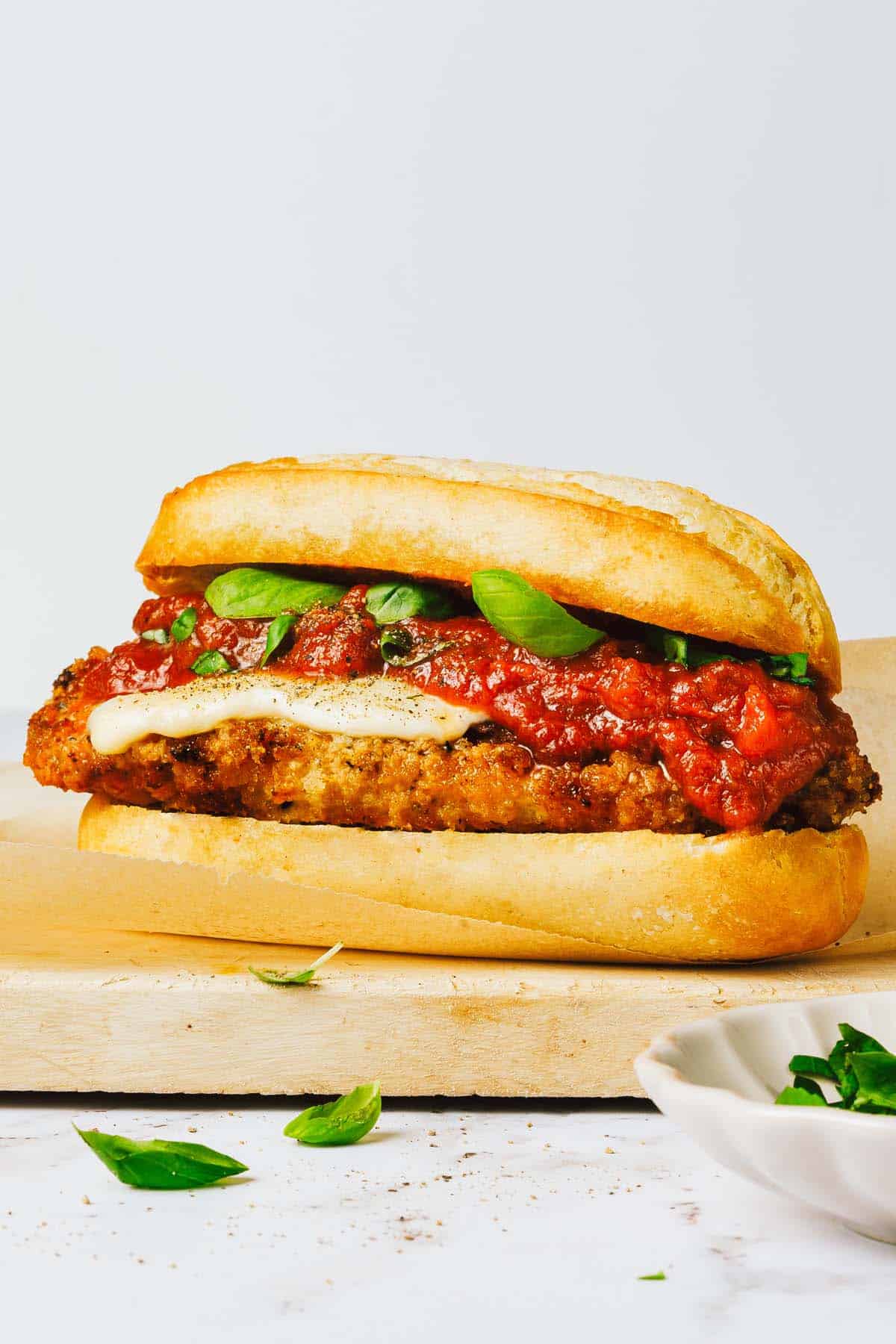 Chicken Parmesan sandwich on a wooden cutting board with fresh basil. 