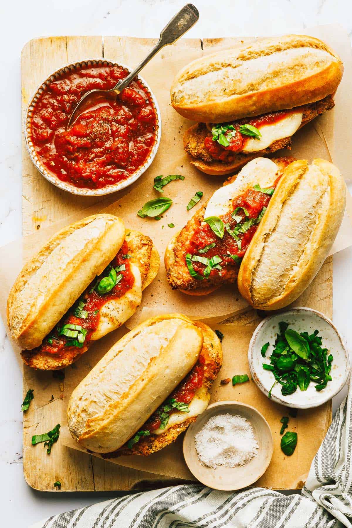 Chicken Parmesan sandwiches on a cutting board with a bowl of marinara. 