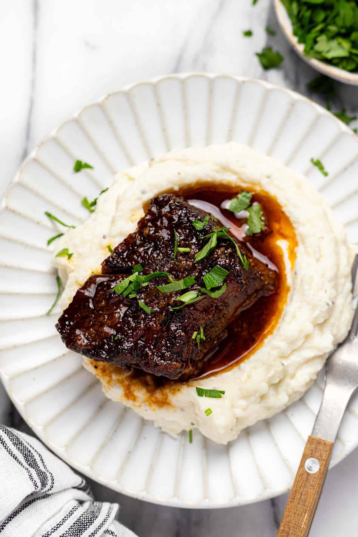 Plate of mashed potatoes topped with a braised beef short rib.