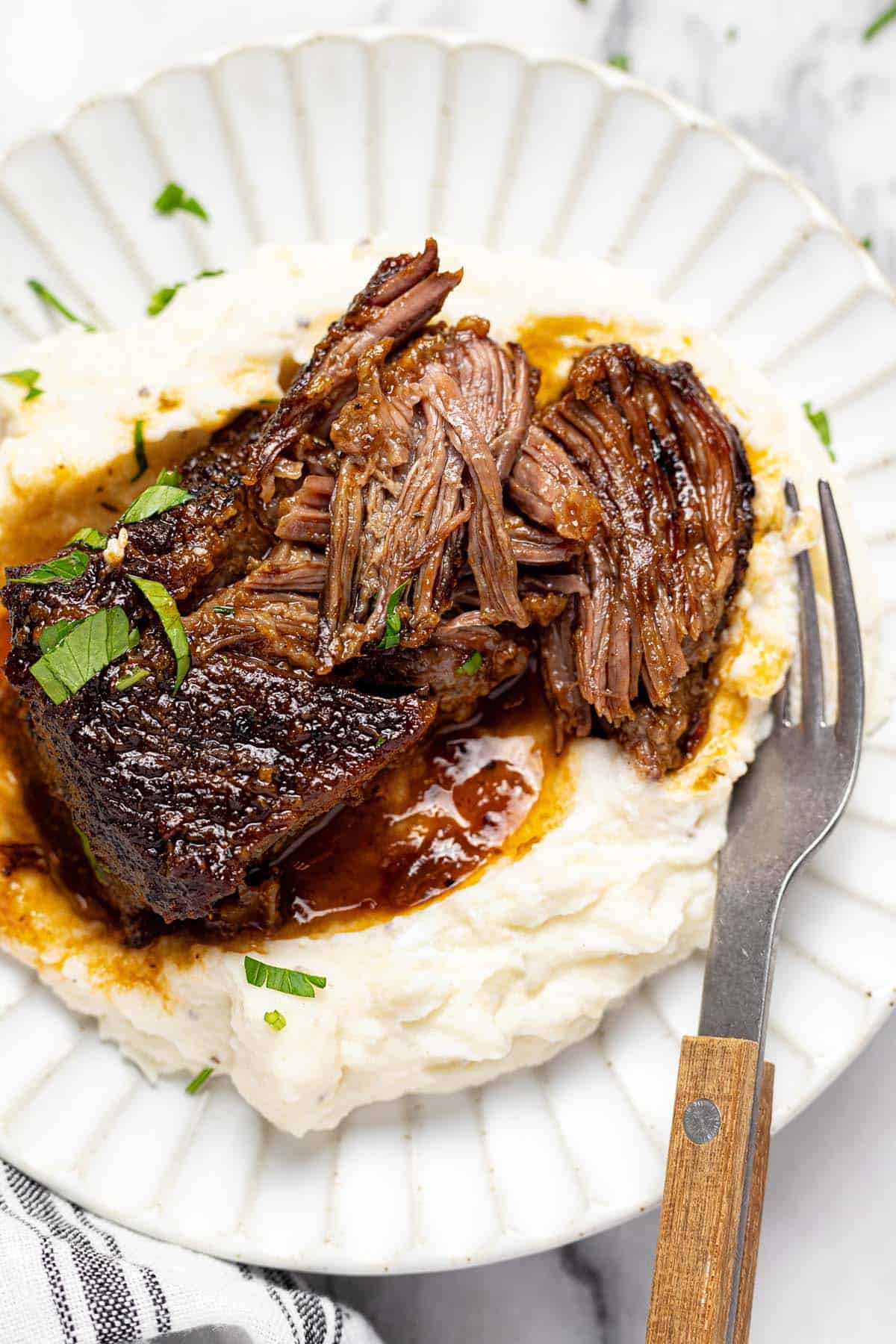 Plate of mashed potatoes topped with shredded braised beef short ribs.