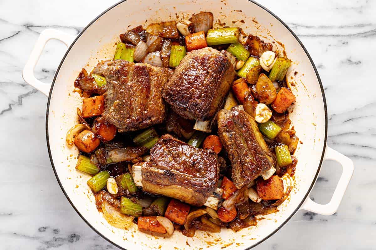 Seared short ribs and sauteed veggies in a pan. 