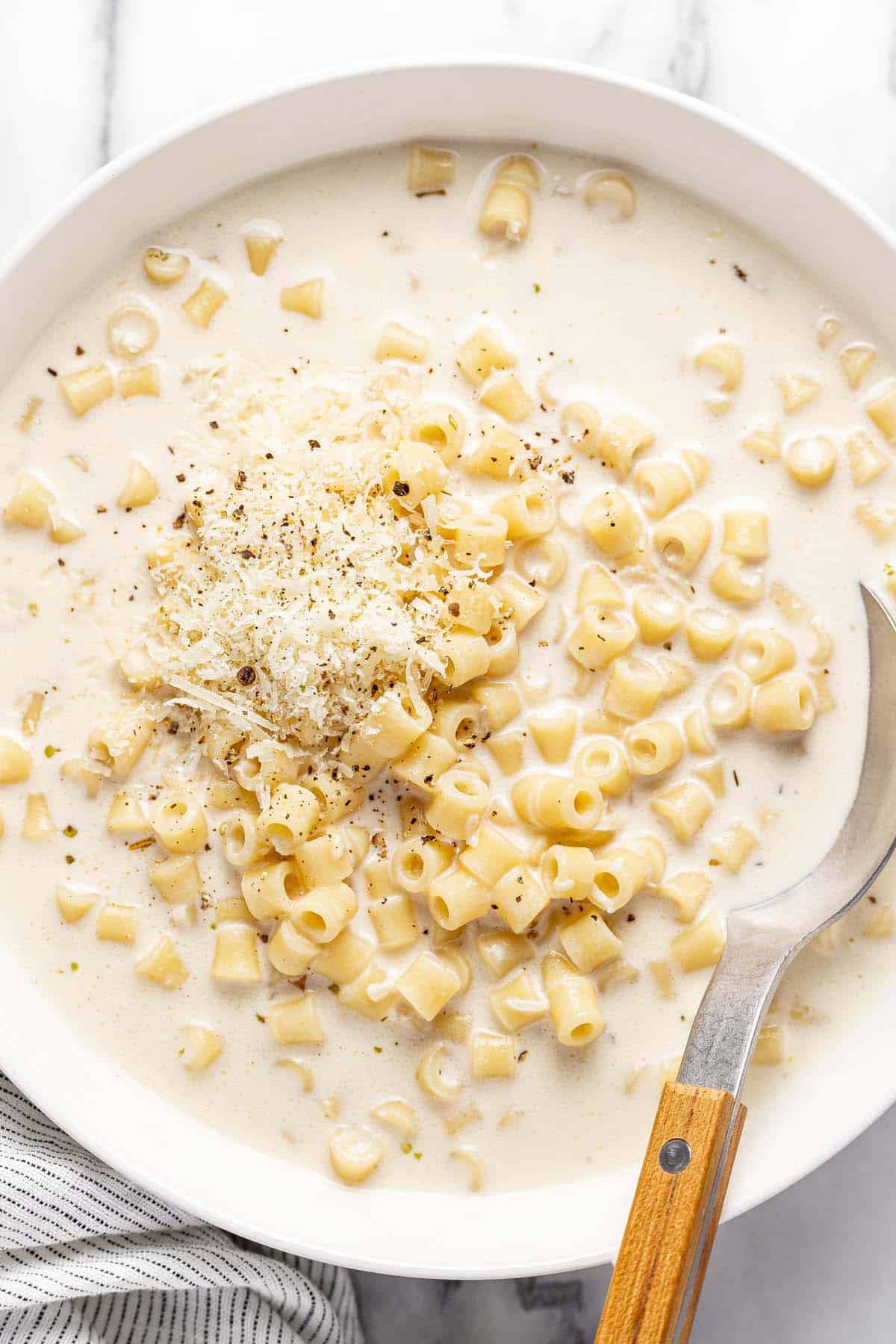 Big bowl of creamy pasta soup garnished with Parmesan and black pepper. 