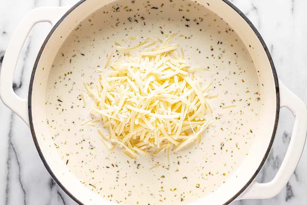 Shredded Parmesan cheese added to a large pot creamy pasta soup. 