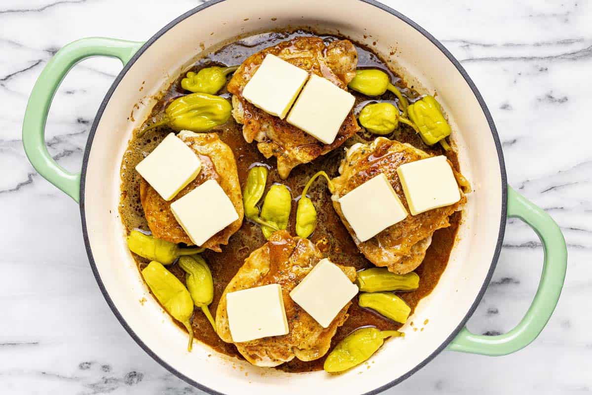 Large pan with sauteed chicken, pepperoncini, and sliced butter. 