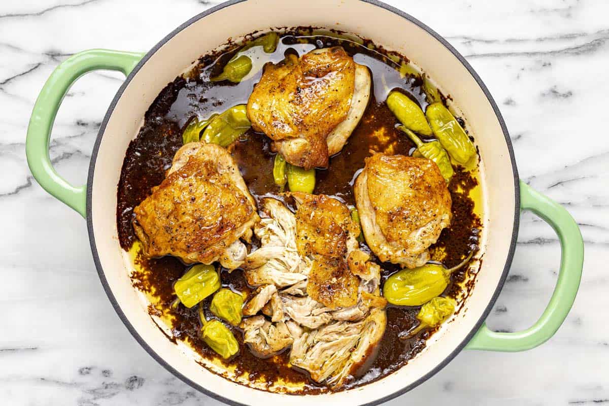 Chicken thighs in a pan with sauce and pepperoncini. 