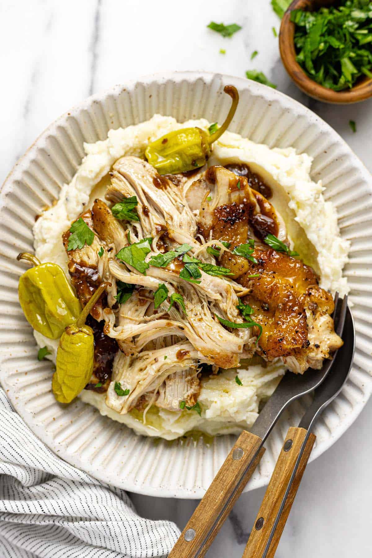 Bowl of shredded chicken thighs with mashed potatoes and pepperoncini. 