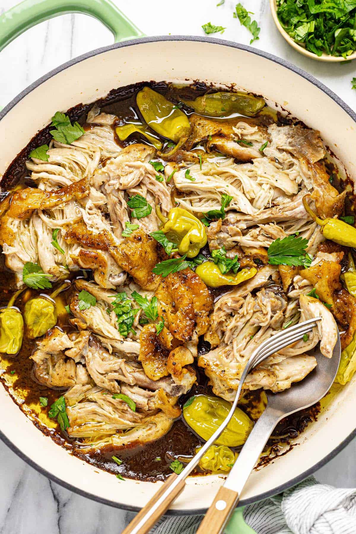 Large pan filled with shredded chicken and pepperoncini garnished with parsley. 