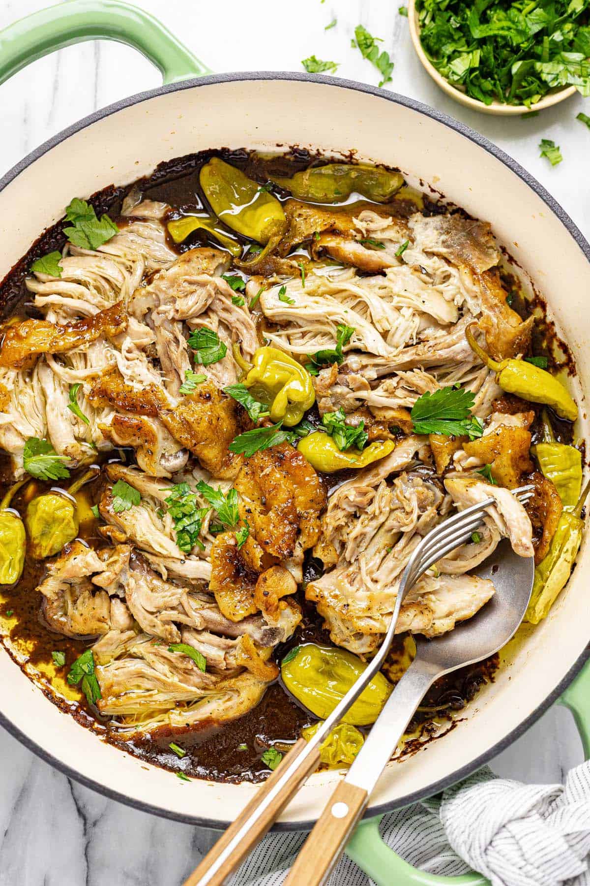 Large pan filled with shredded chicken and pepperoncini garnished with parsley. 