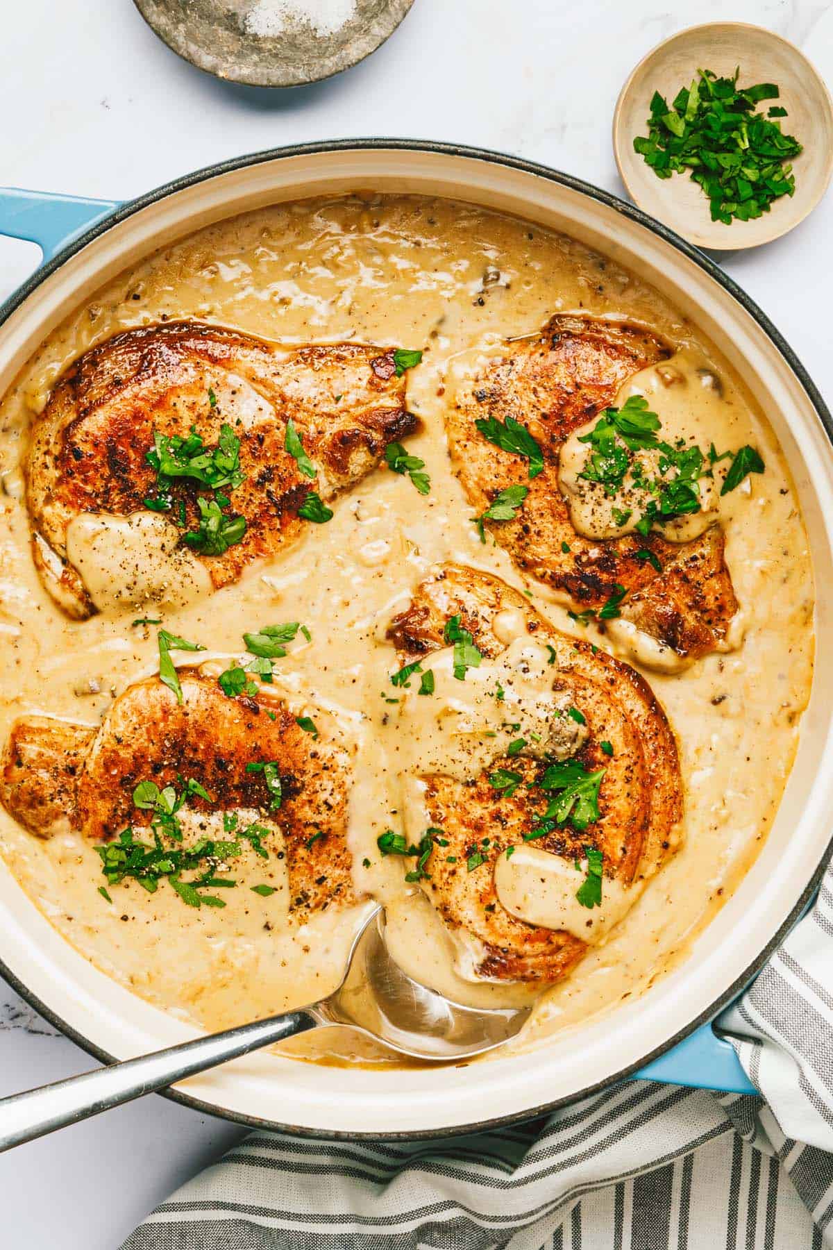 Large pan filled with seared pork chops in creamy mushroom sauce. 