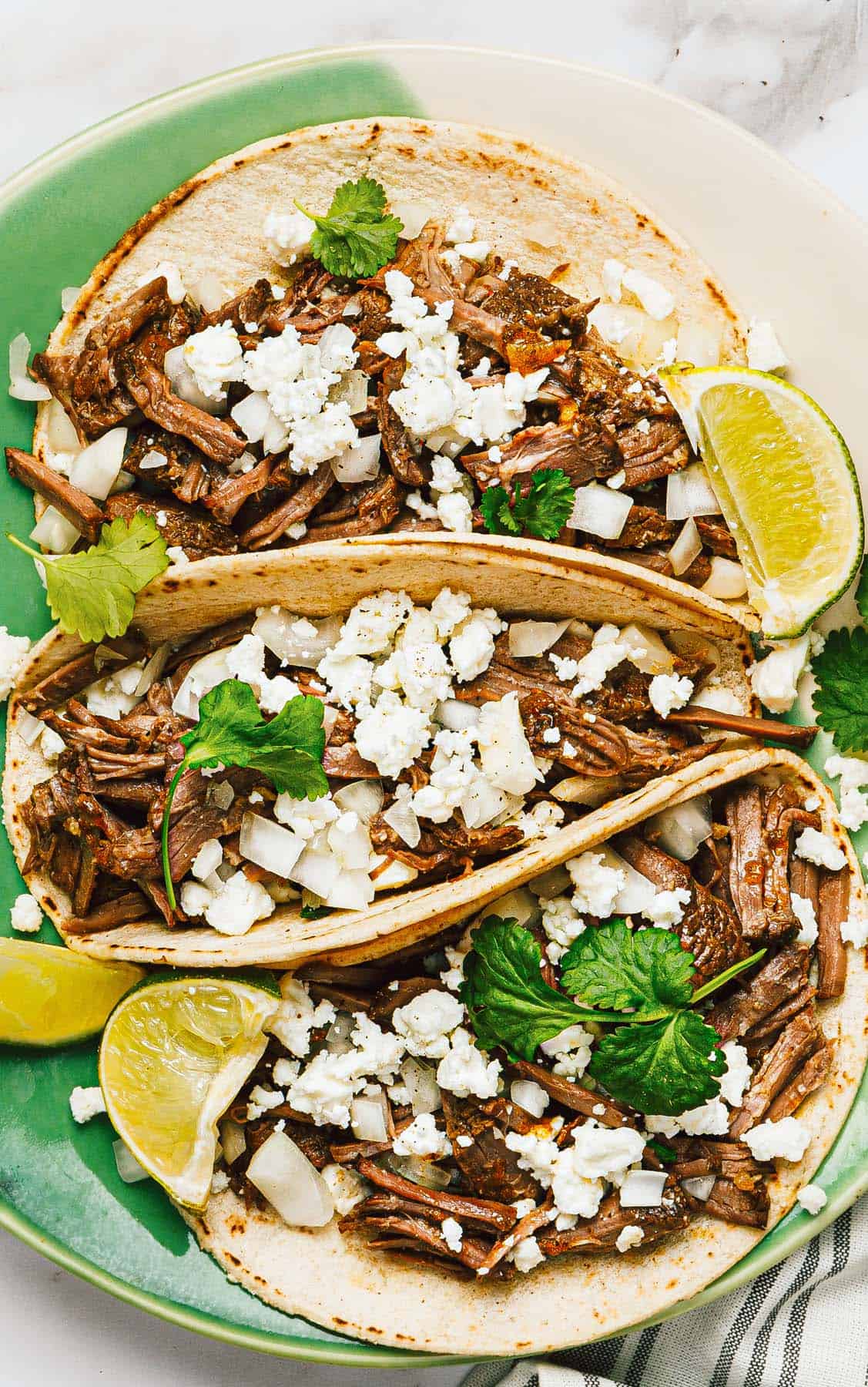 Plate with 3 shredded beef tacos topped with Cotija cheese. 