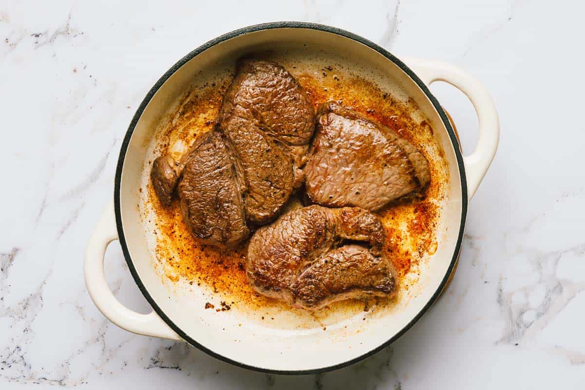 Large pan with seared beef in it. 