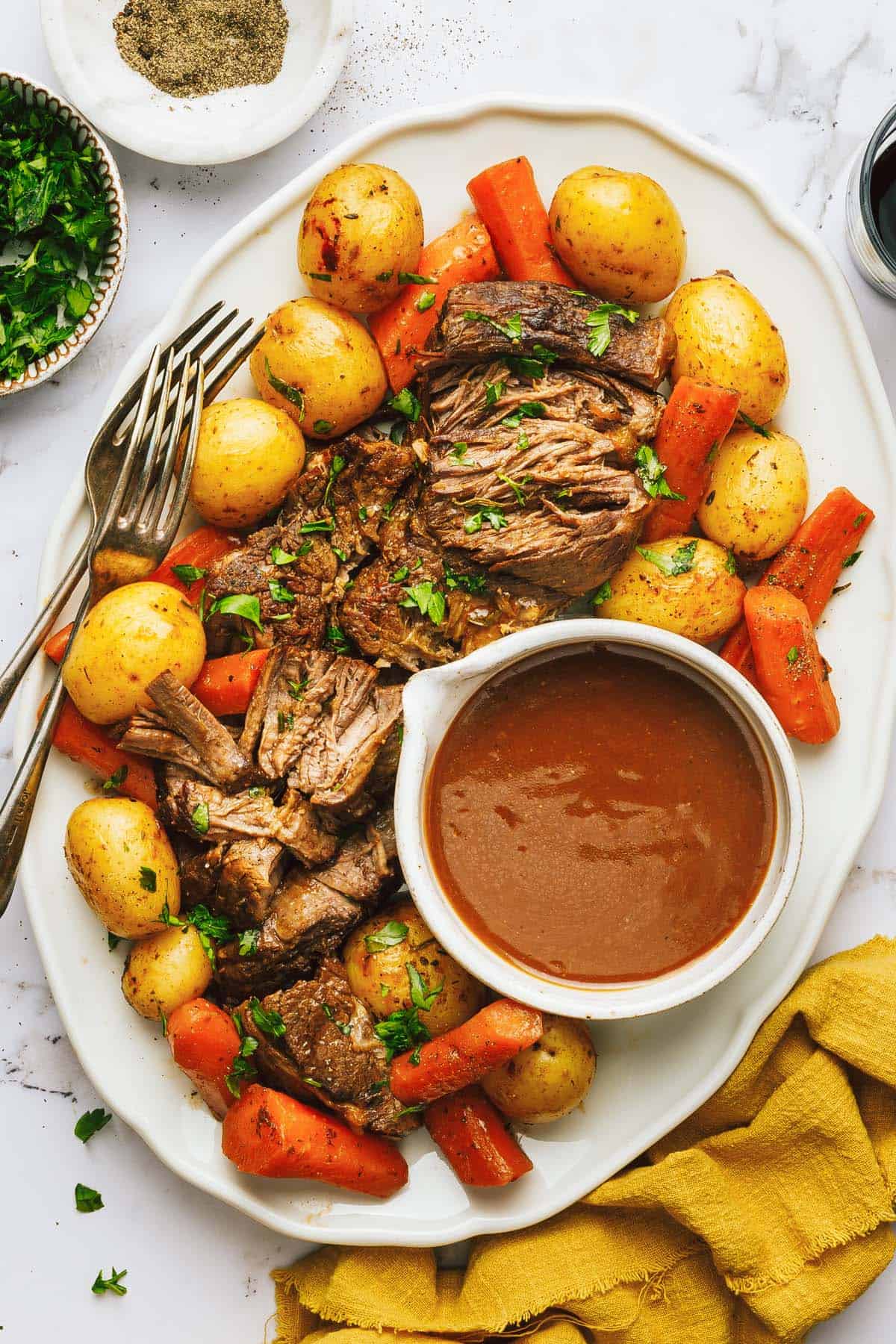 Large platter with pot roast, potatoes, carrots, and gravy garnished with parsley. 