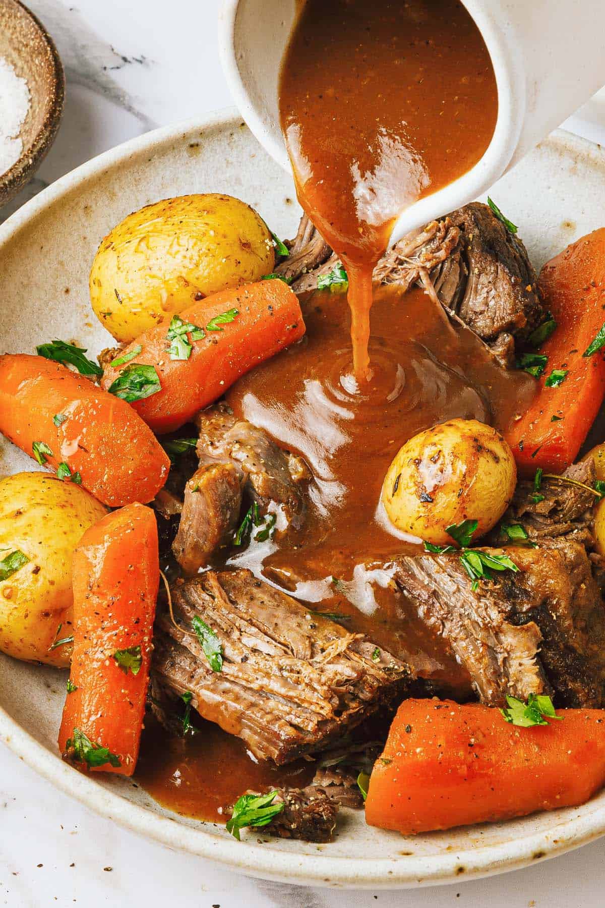 Beef gravy being poured over a Dutch oven pot roast. 