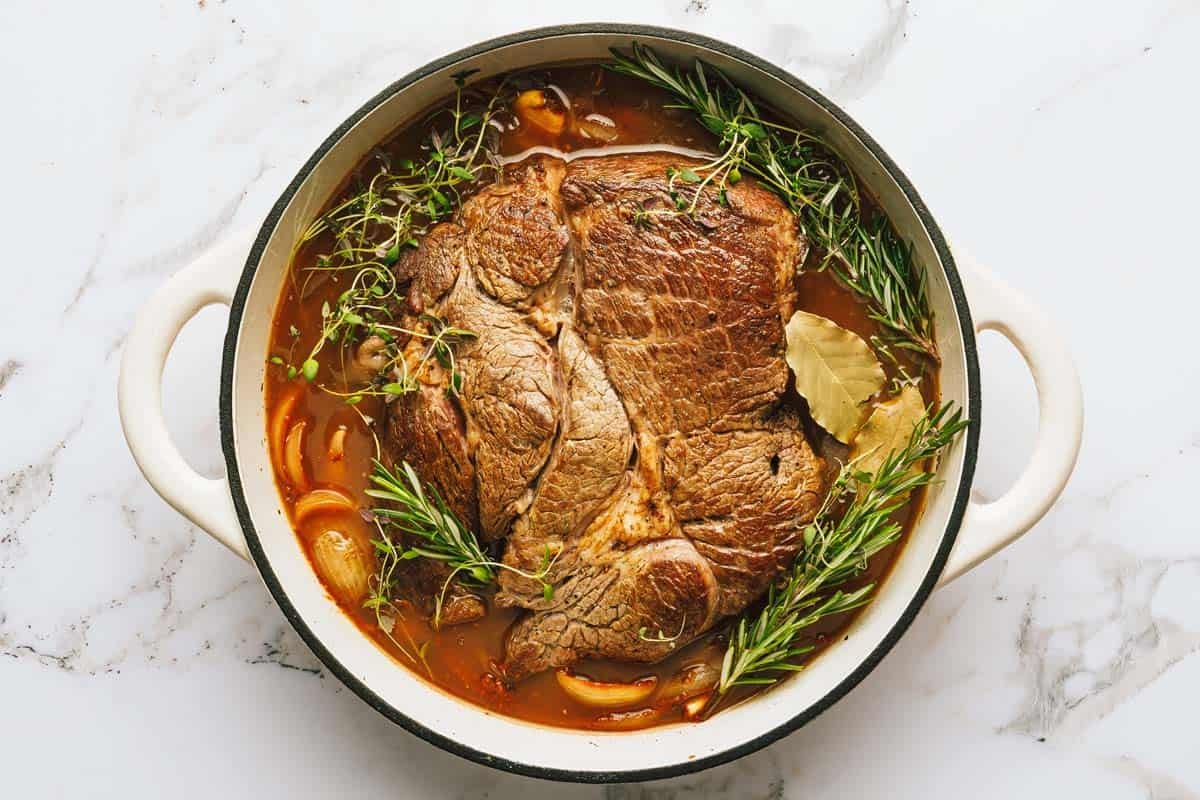 Seared roast with herbs and stock in a large pot. 