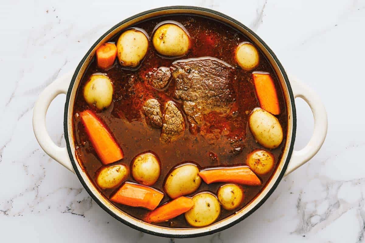 Potatoes and carrots being added to a Dutch oven with a pot roast. 