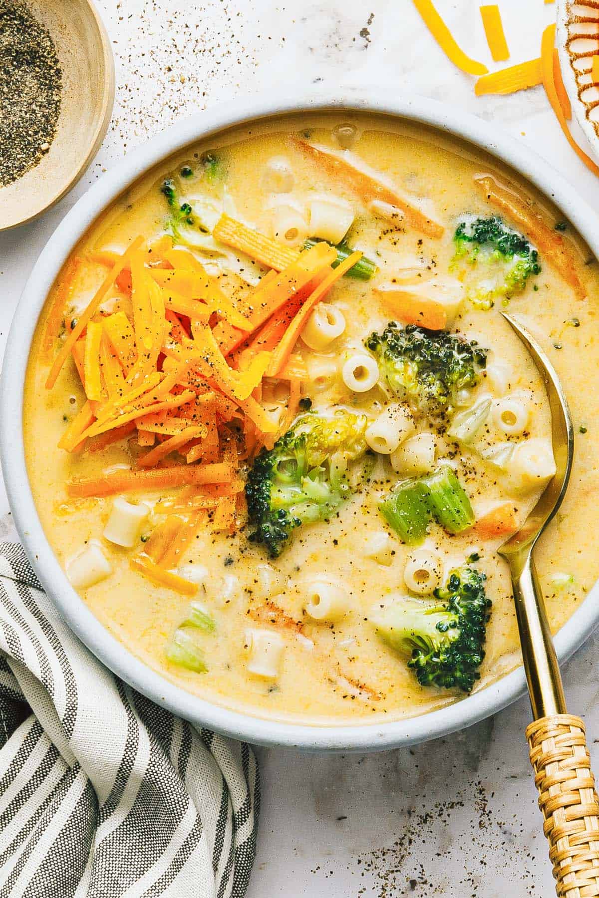 Bowl of cheesy broccoli soup with noodles topped with cheddar. 