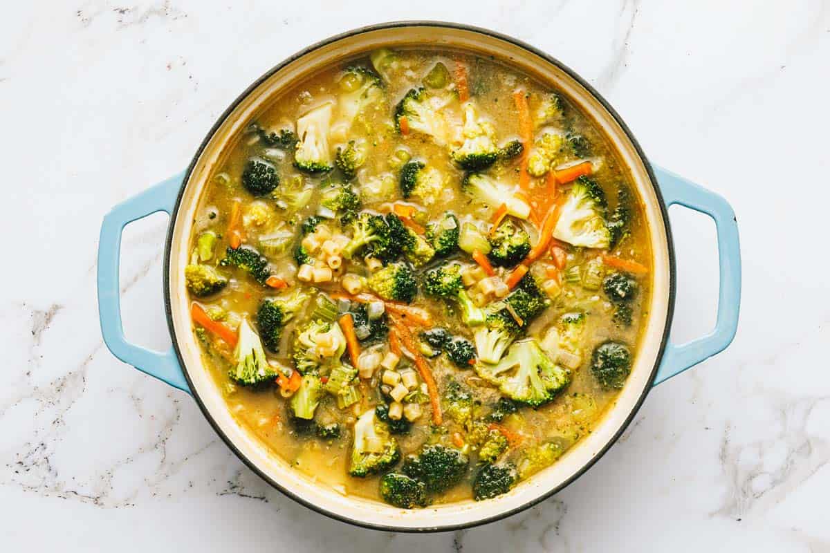 Veggies and noodles cooking in a broth in a large pot. 