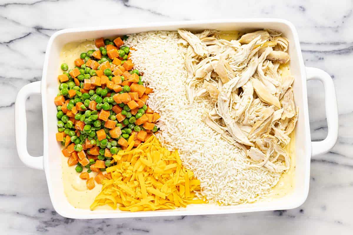 Veggies, cheese, rice, and chicken in a baking dish with sauce. 