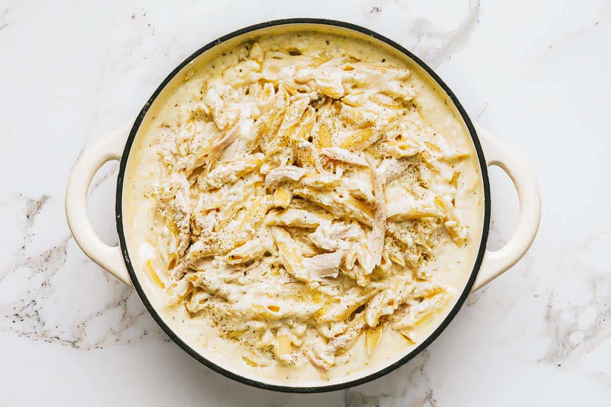 Pasta, chicken, and alfredo sauce mixed together in a large pan. 