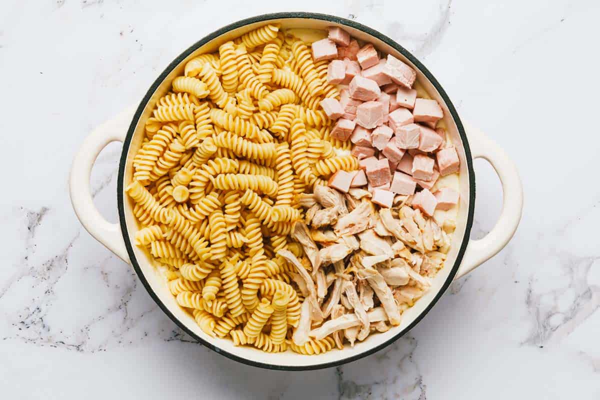 Large pan with pasta, ham, chicken, and cream sauce. 