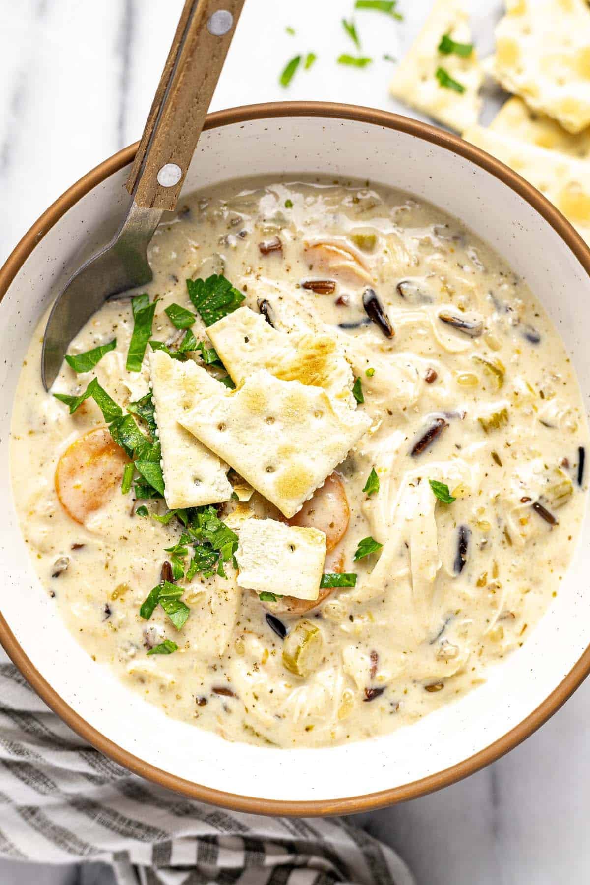 Bowl of chicken wild rice soup topped with parsley and crackers. 