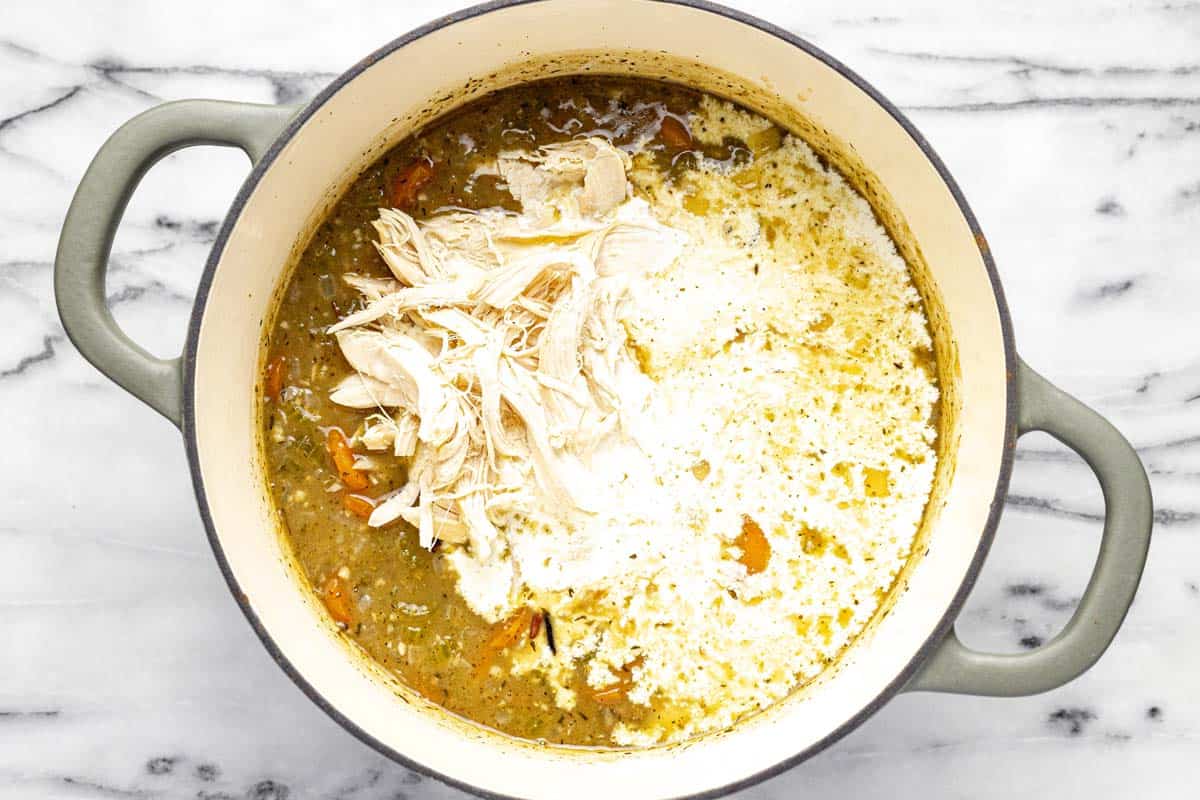 Shredded chicken and heavy cream being added to a large pot of soup. 