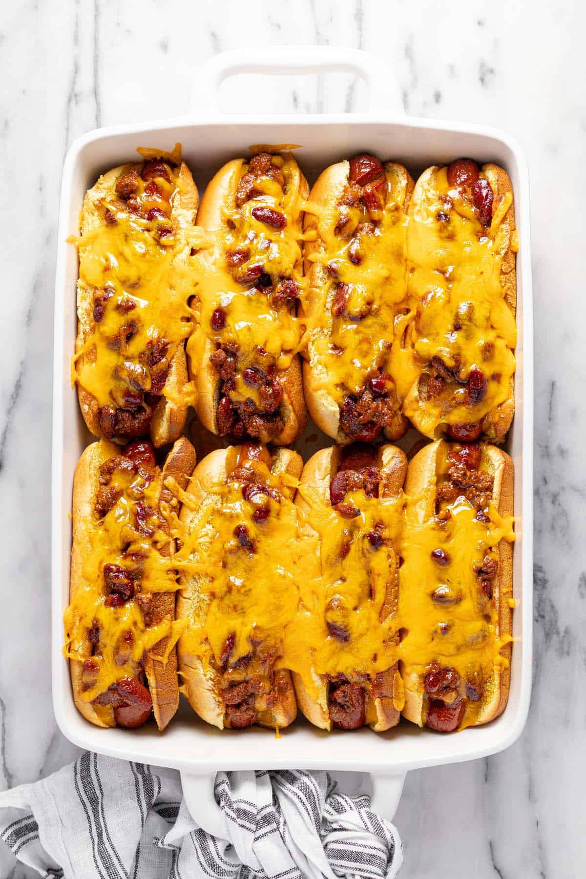 Freshly baked chili cheese dogs in  a large baking dish. 