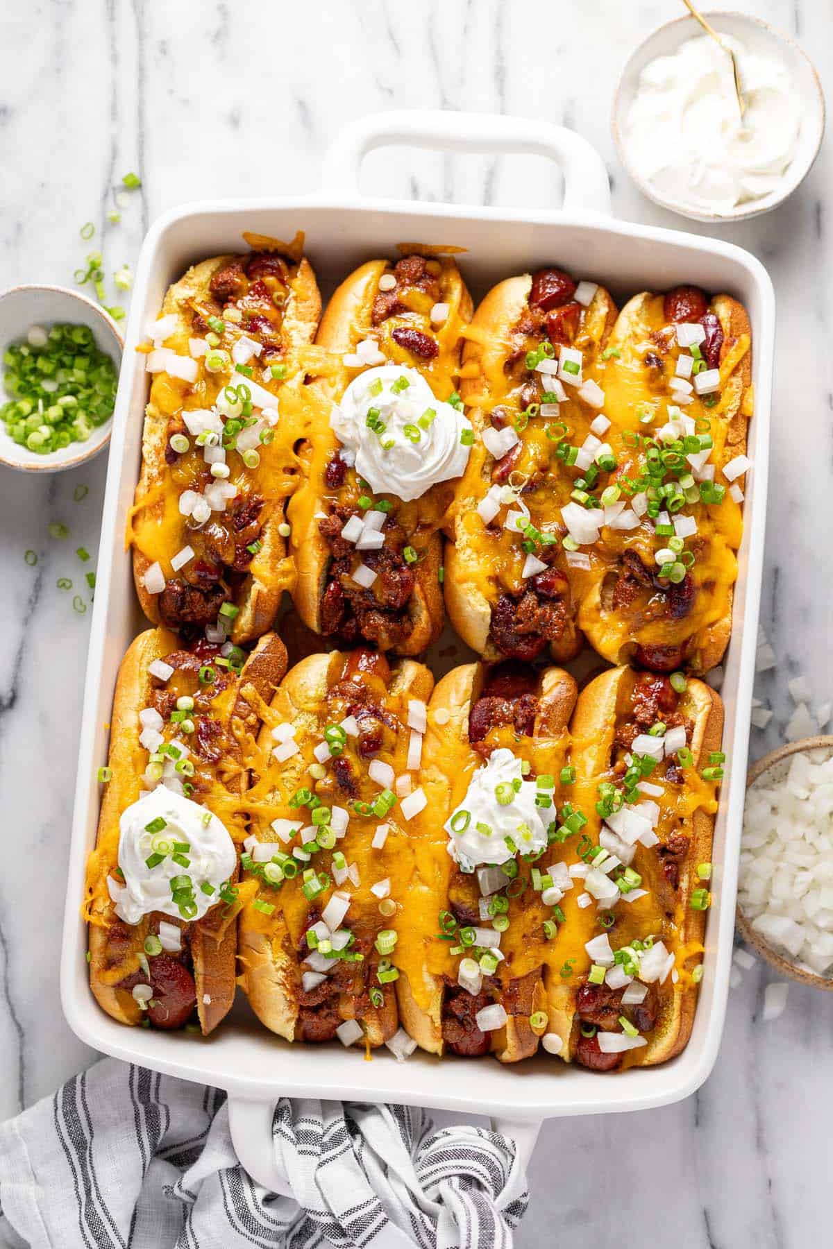 Baking dish filled with chili cheese dogs topped with onions. 