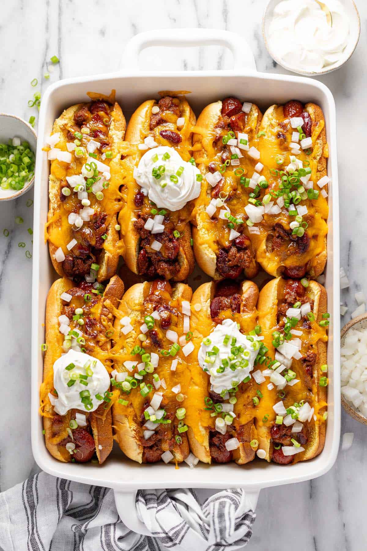 Baking dish filled with chili cheese dogs topped with onions and sour cream. 