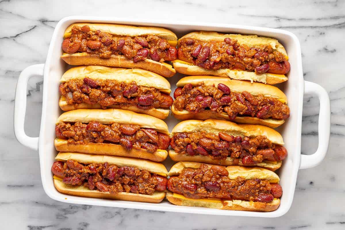 Chili on top of hot dogs in buns in a baking dish. 