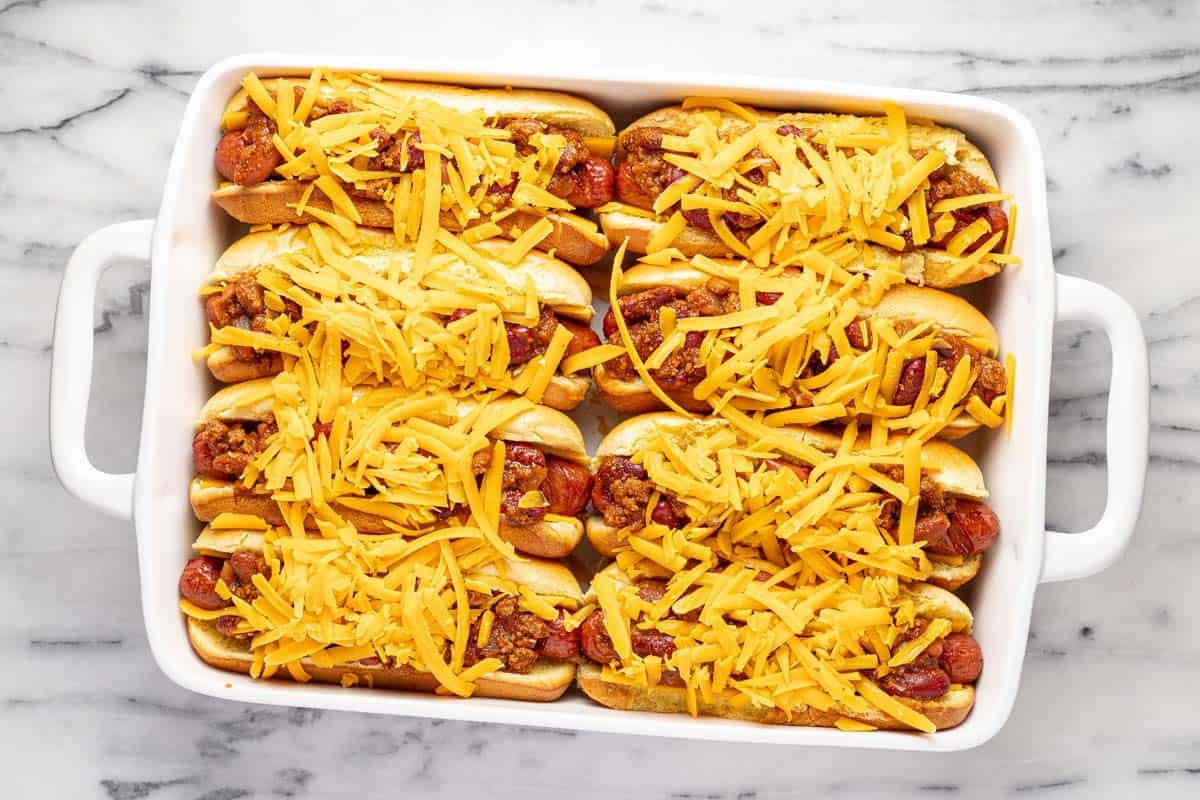 Chili dogs topped with cheese in a large baking dish. 