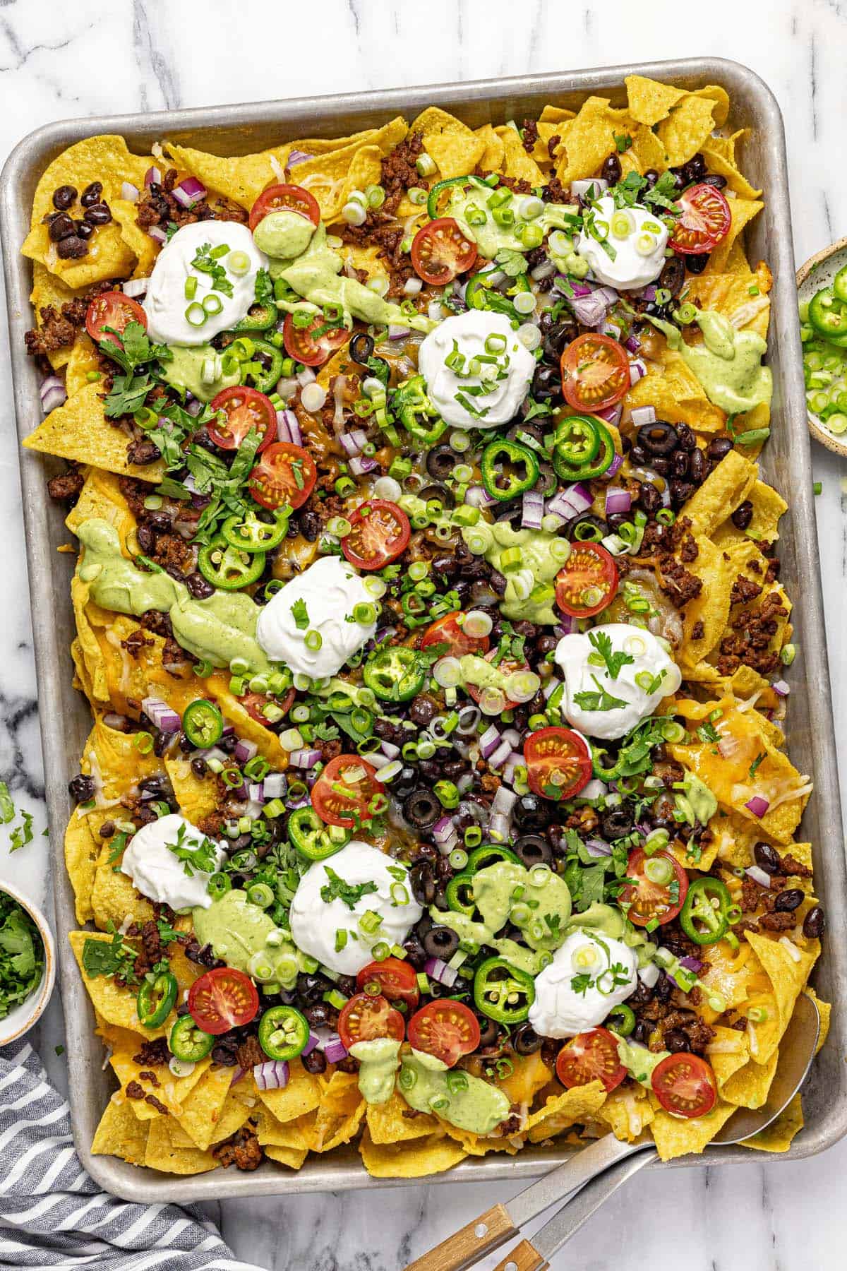 Sheet pan filled with loaded nachos topped with sour cream. 