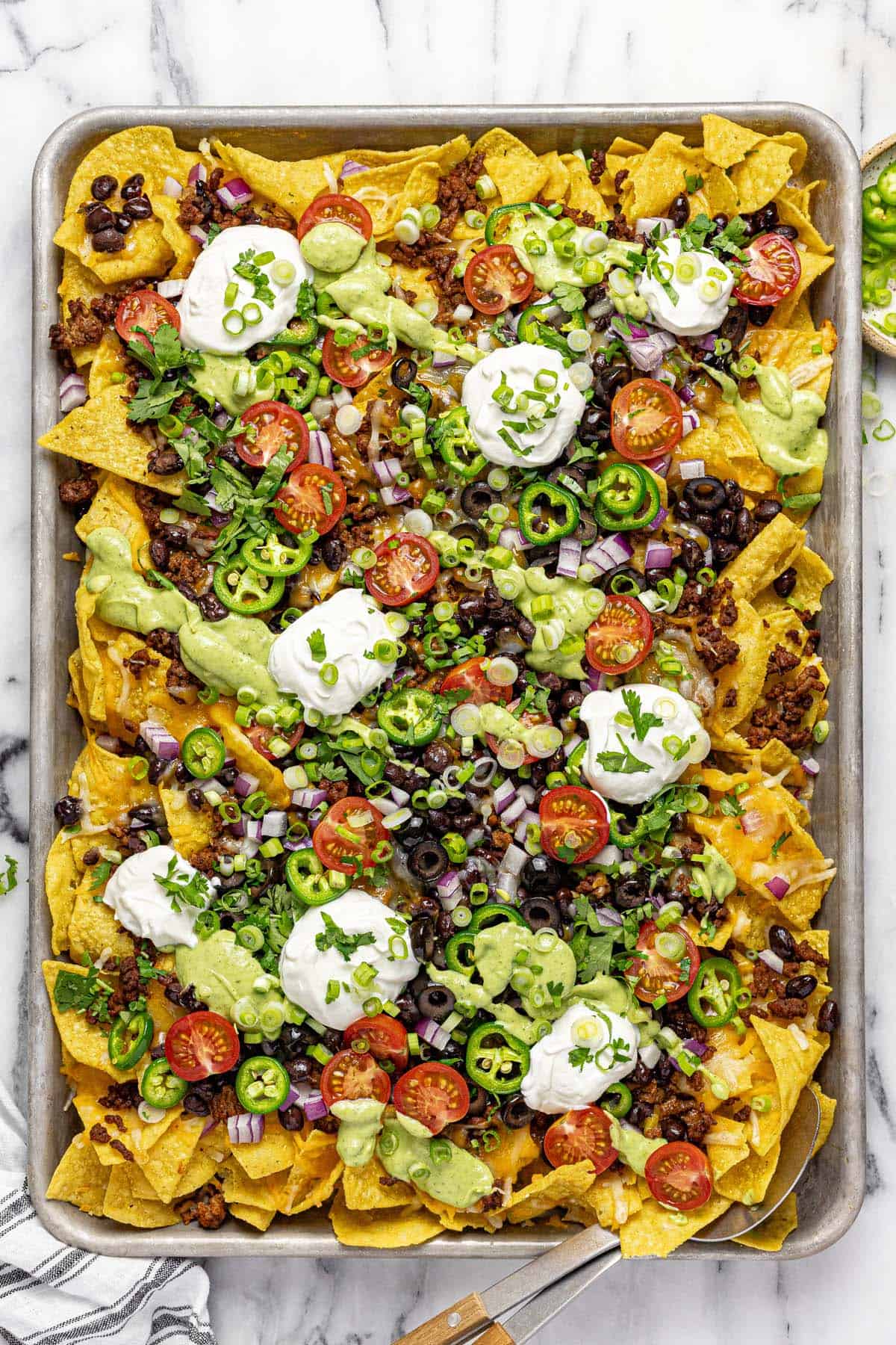 Sheet pan filled with loaded nachos topped with sour cream. 